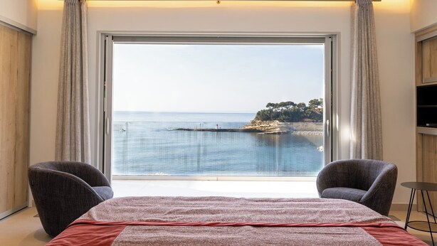 A bedroom with a large bed, two armchairs, a TV, and a view of the sea. - Villa de Luxe Front de Mer Avec Piscine villa Romanella (Carry-le-Rouet)