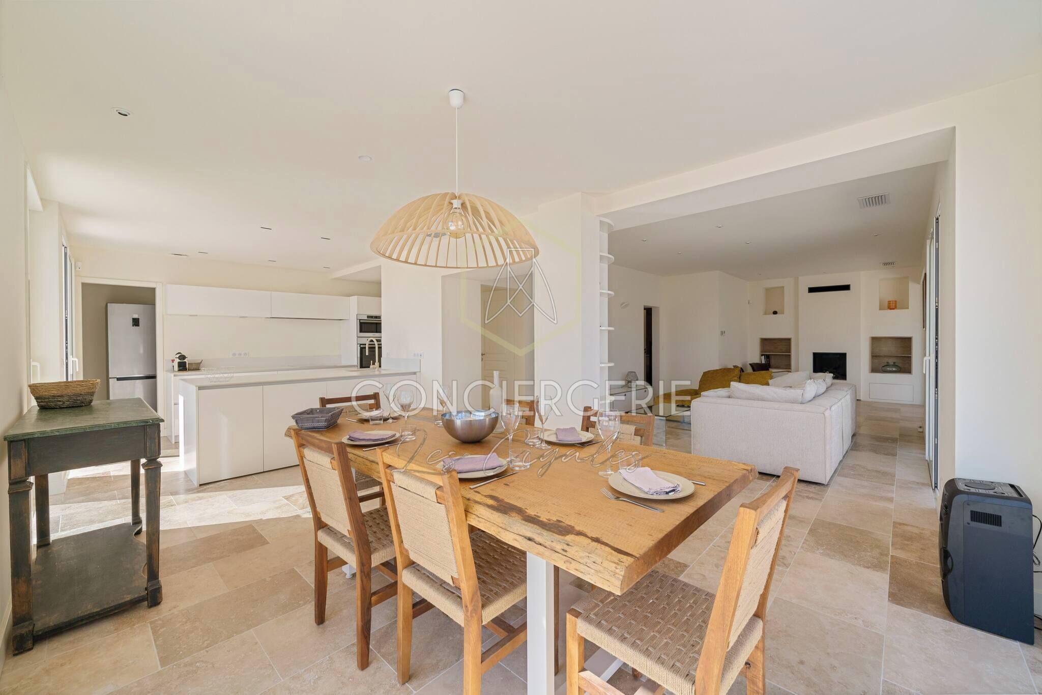 Una cocina moderna con armarios blancos, un comedor con mesa de madera preparada para cuatro personas y una sala de estar con un sofá blanco.