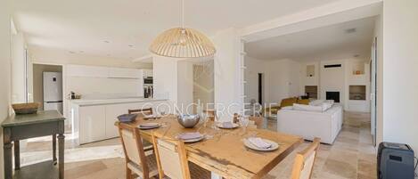 Una cocina moderna con armarios blancos, un comedor con mesa de madera preparada para cuatro personas y una sala de estar con un sofá blanco.