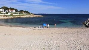 En strand med klart vand, et par mennesker og huse i baggrunden.