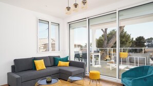Een moderne woonkamer met een grijze hoekbank, gele en groene kussens, twee ronde tafels met gouden randen, en een fauteuil in turquoise.