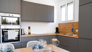 Een moderne keuken met grijze kastjes, een ingebouwde oven en een eethoek met een houten tafel voor vier personen.