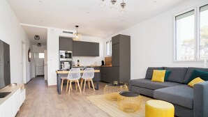 Een moderne woonkamer met een grijze bank, een geel poef en een eethoek met een tafel en stoelen.
