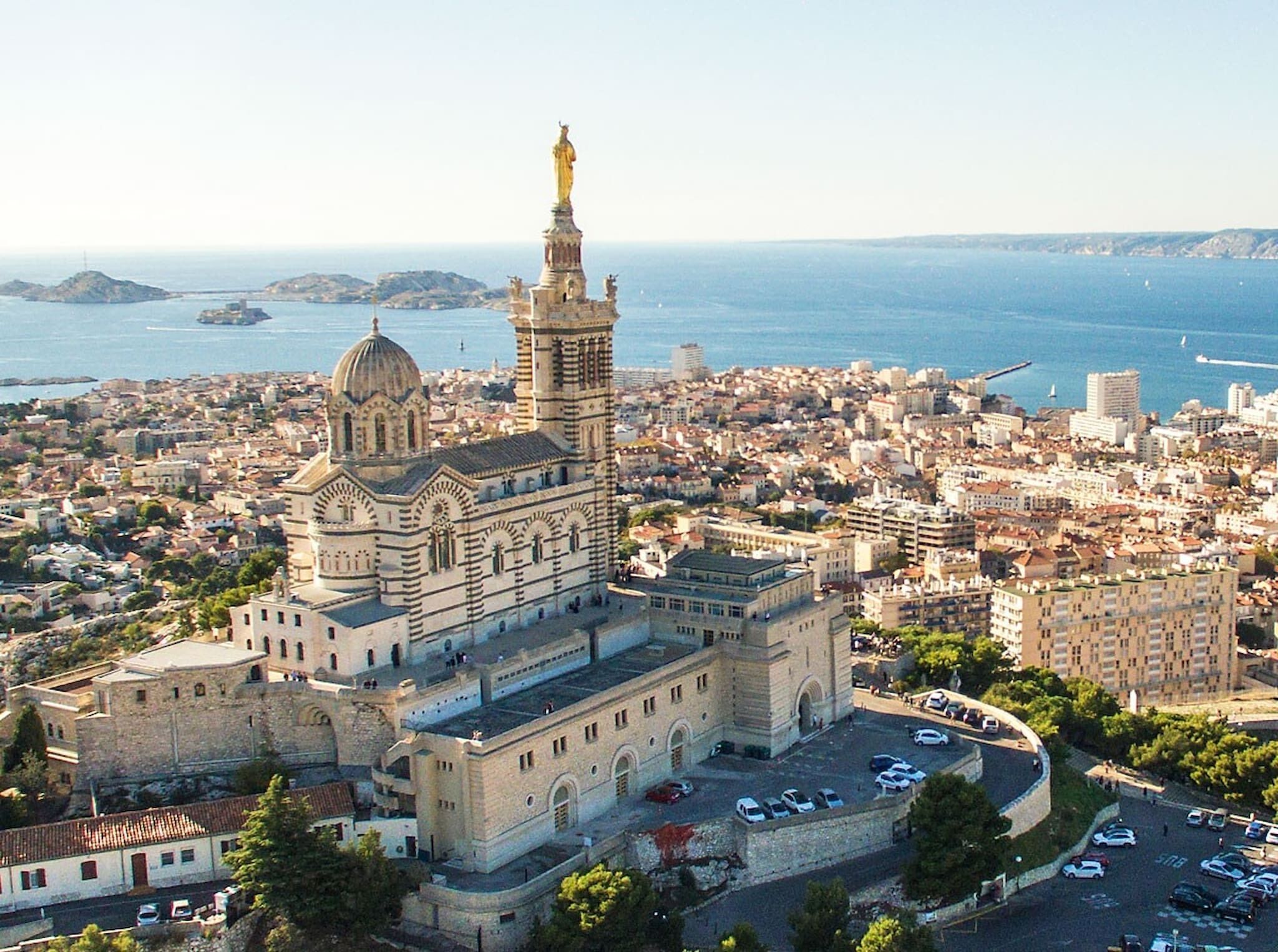 Vista aerea di un edificio storico con una cupola imponente e una statua sulla sommità, immerso in un'area urbana densamente popolata con strade e auto parcheggiate.