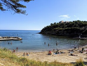 En strand med folk som badar och solar, en klippig kustlinje och byggnader på en kulle.