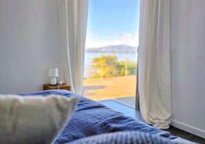 A bedroom with a bed, a nightstand with a lamp, and a view of a body of water and greenery through a window. - Large family villa, exceptional panoramic sea view (Coti chiavari)