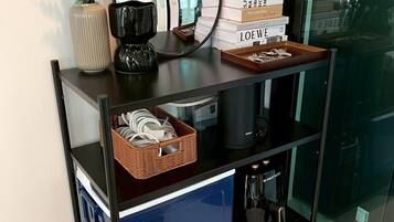 A black metal console table with a mirror, a vase with green foliage, a stack of books, and a tray with keys.