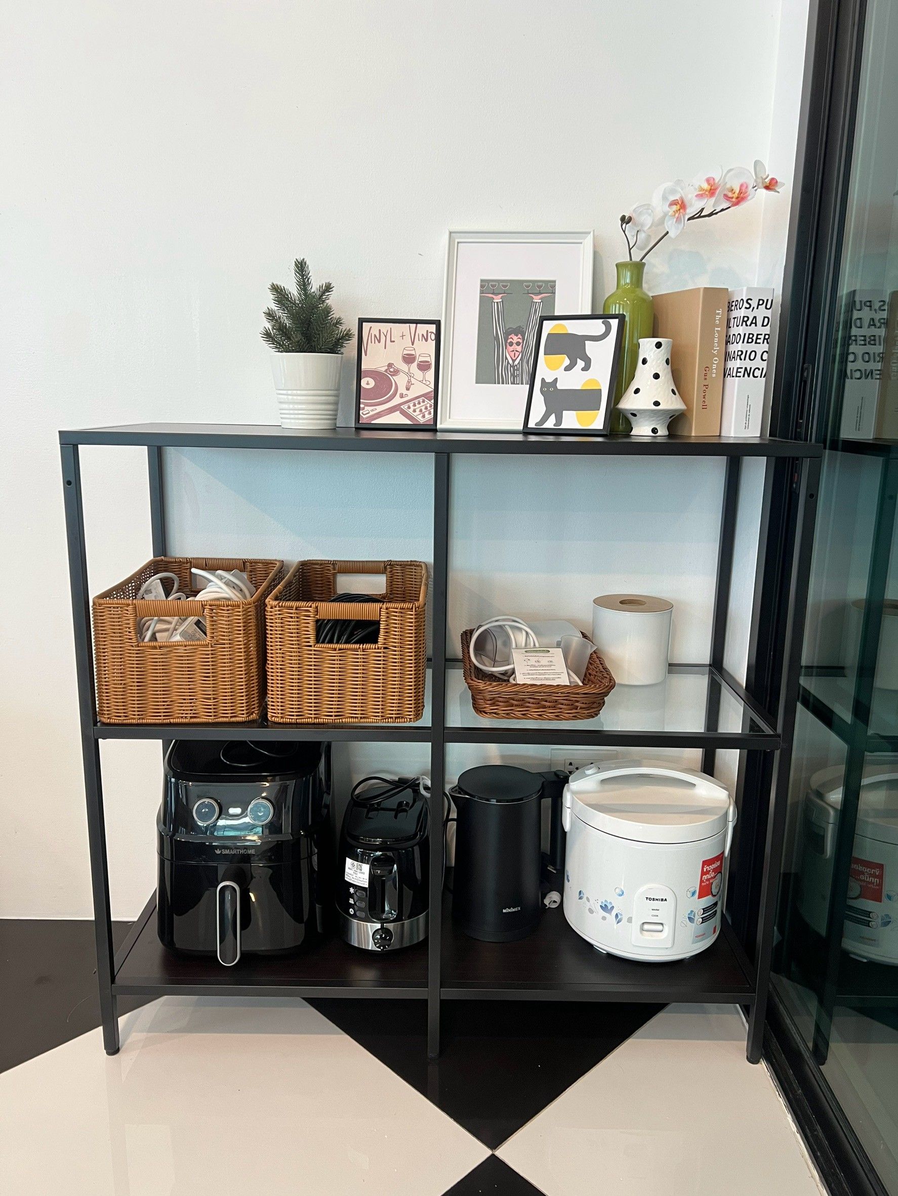 A black-framed shelf with wicker baskets, a coffee maker, a kettle, and a rice cooker.