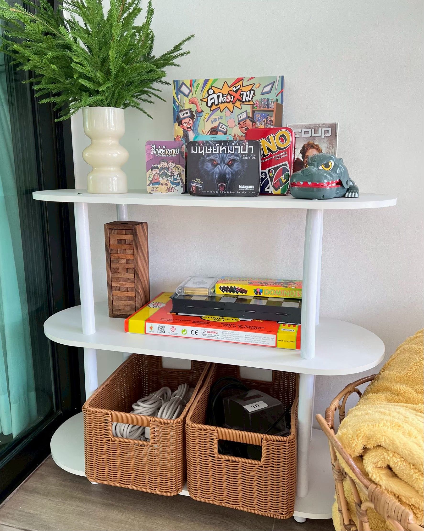 Une étagère avec divers jeux de société et une plante en pot.