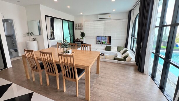 A modern living room with a dining area, large windows, and a view of a swimming pool. - V Villa Khaoyai (Pak Chong)