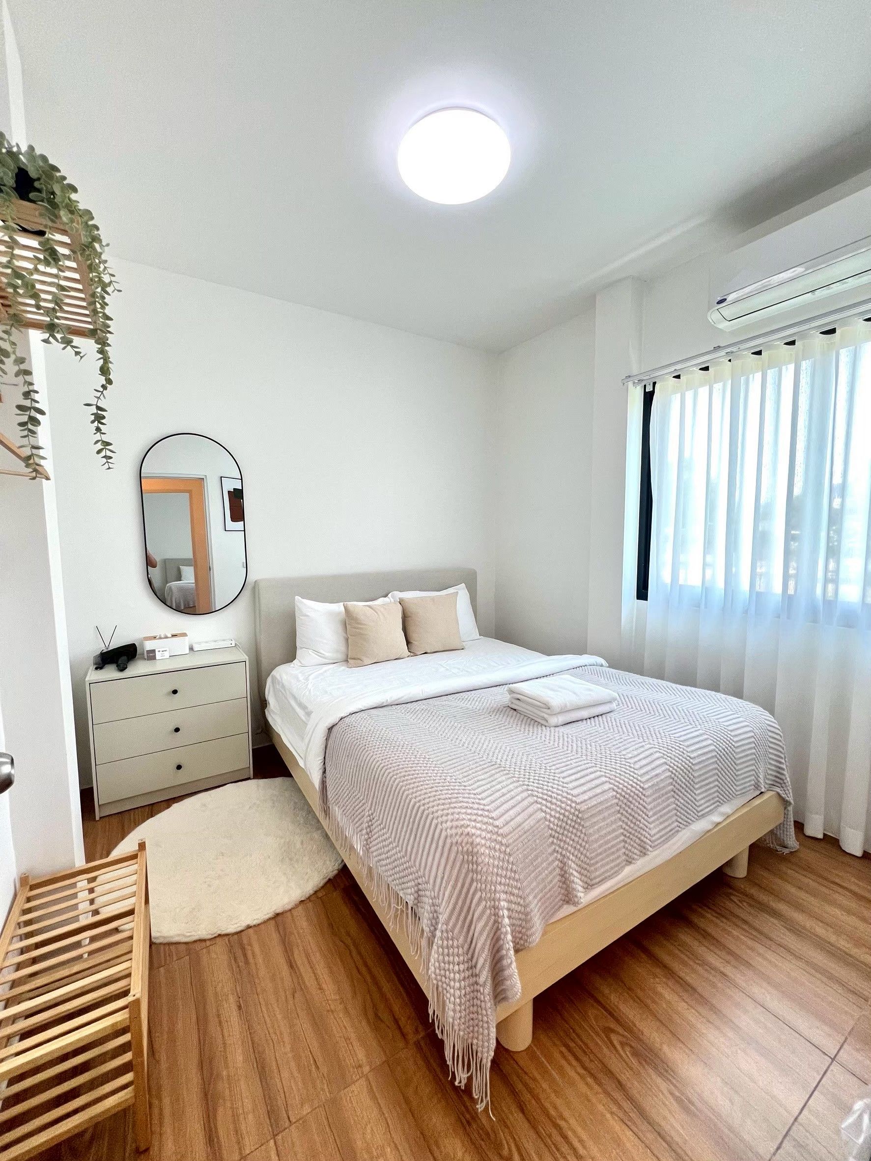 A bedroom with a bed, bedside table, mirror, and a window with curtains.