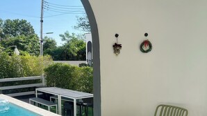 Zona junto a la piscina con una mesa y dos sillas, una mesita pequeña y un adorno decorativo en la pared.