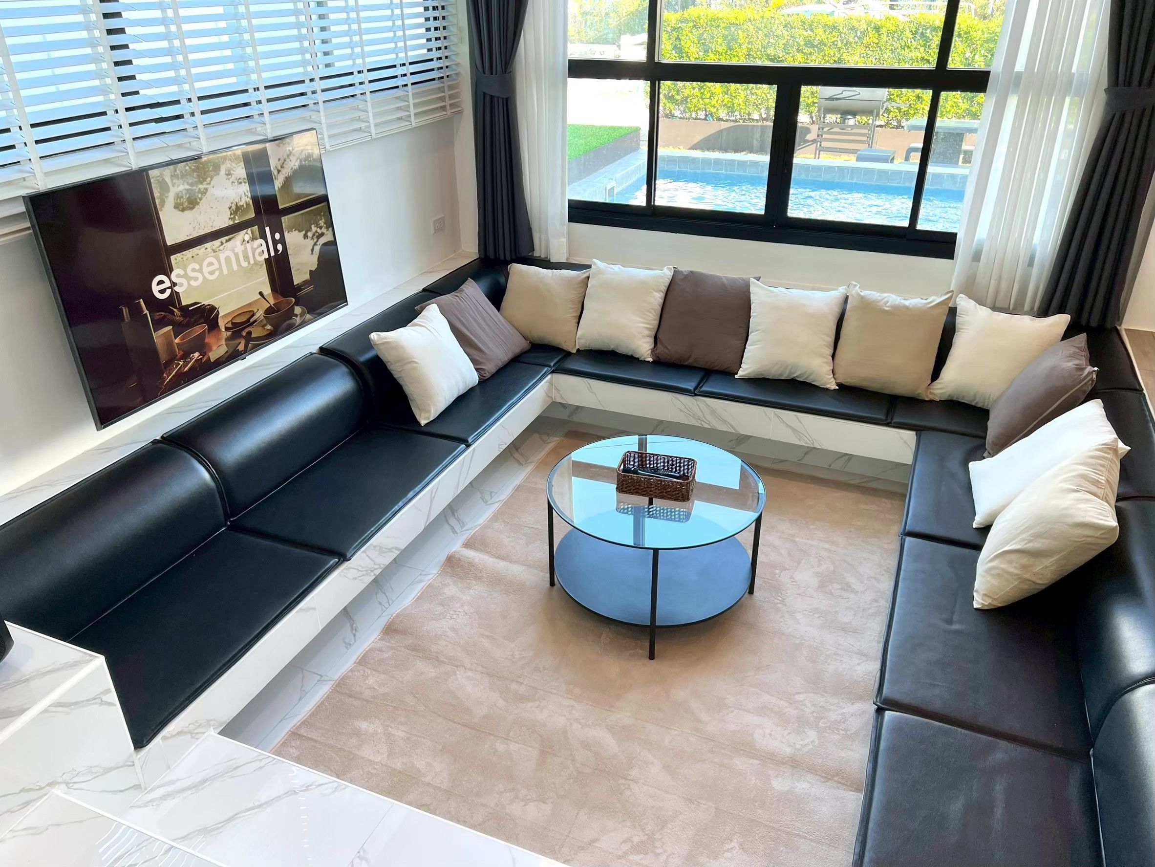 A modern living room with a sectional sofa, a glass coffee table, and a large window with a view of a swimming pool.