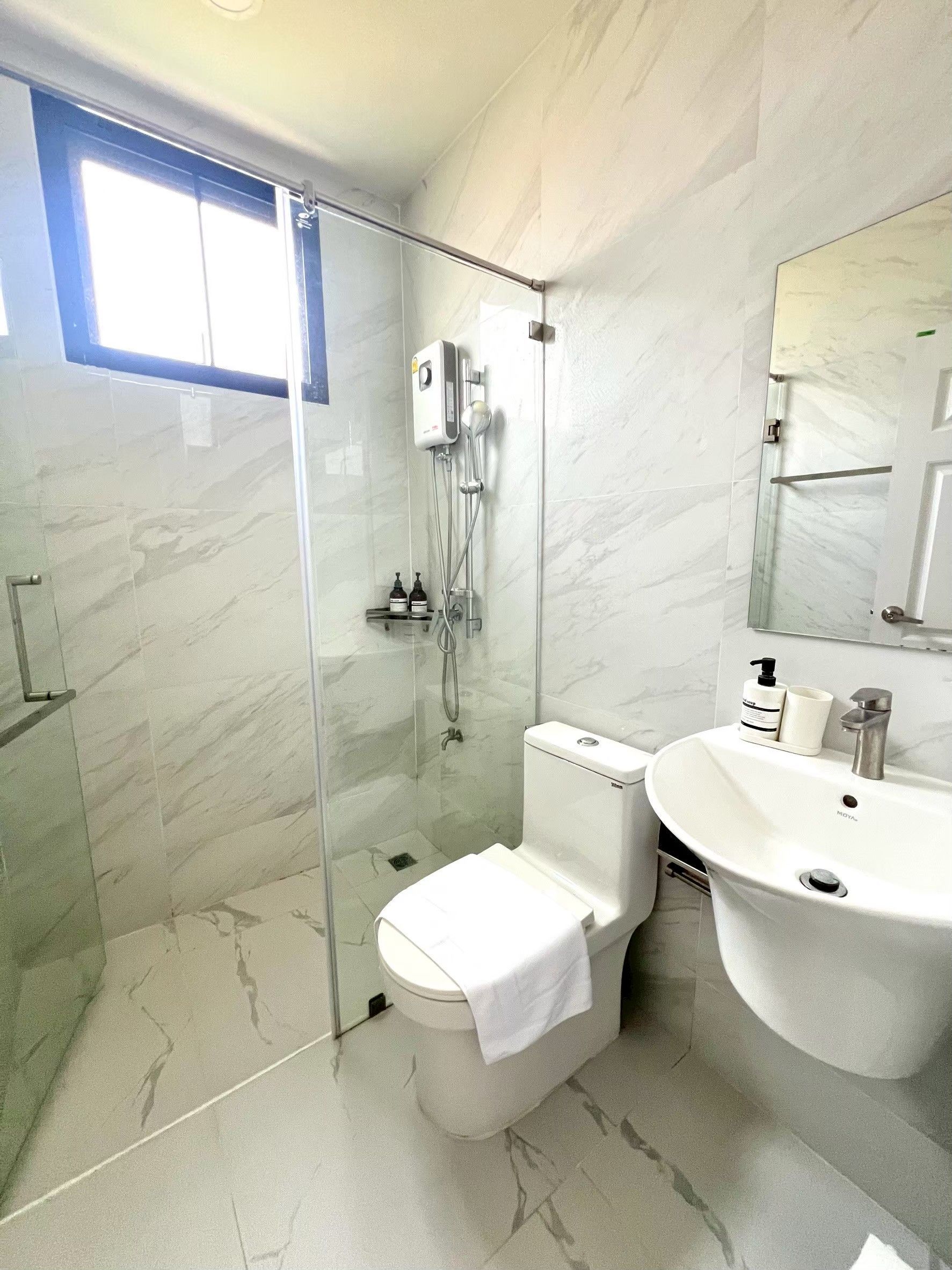 Un baño moderno con ducha envuelta en vidrio, inodoro y lavamanos con espejo superior.