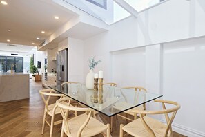 A modern kitchen with a glass dining table and wicker chairs, a stainless steel refrigerator, and a large window. - Architectural Redfern Gem – Designer 3BR Home with Courtyard & Loft (Redfern)