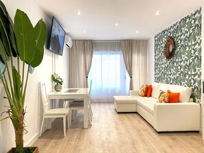 Ein modernes Wohnzimmer mit einem weißen Sofa, einem Esstisch mit Stühlen und einer großen Kübelpflanze.
