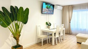 Uma sala de estar moderna com área de jantar, uma grande planta em vaso, uma televisão de tela plana na parede e uma janela com cortinas.