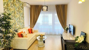 Uma sala de estar com sofá, mesa de centro, TV e vista para uma varanda.