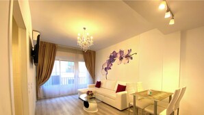 Uma sala de estar moderna com um sofá branco, uma mesa de jantar com cadeiras, um lustre e uma grande janela com cortinas.