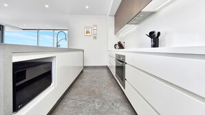 A modern kitchen with a built-in oven, a microwave, and a stainless steel range hood. - Oceanview Penthouse Caves Beach (Caves Beach)