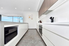 A modern kitchen with a built-in oven, a microwave, and a stainless steel range hood. - Oceanview Penthouse Caves Beach (Caves Beach)