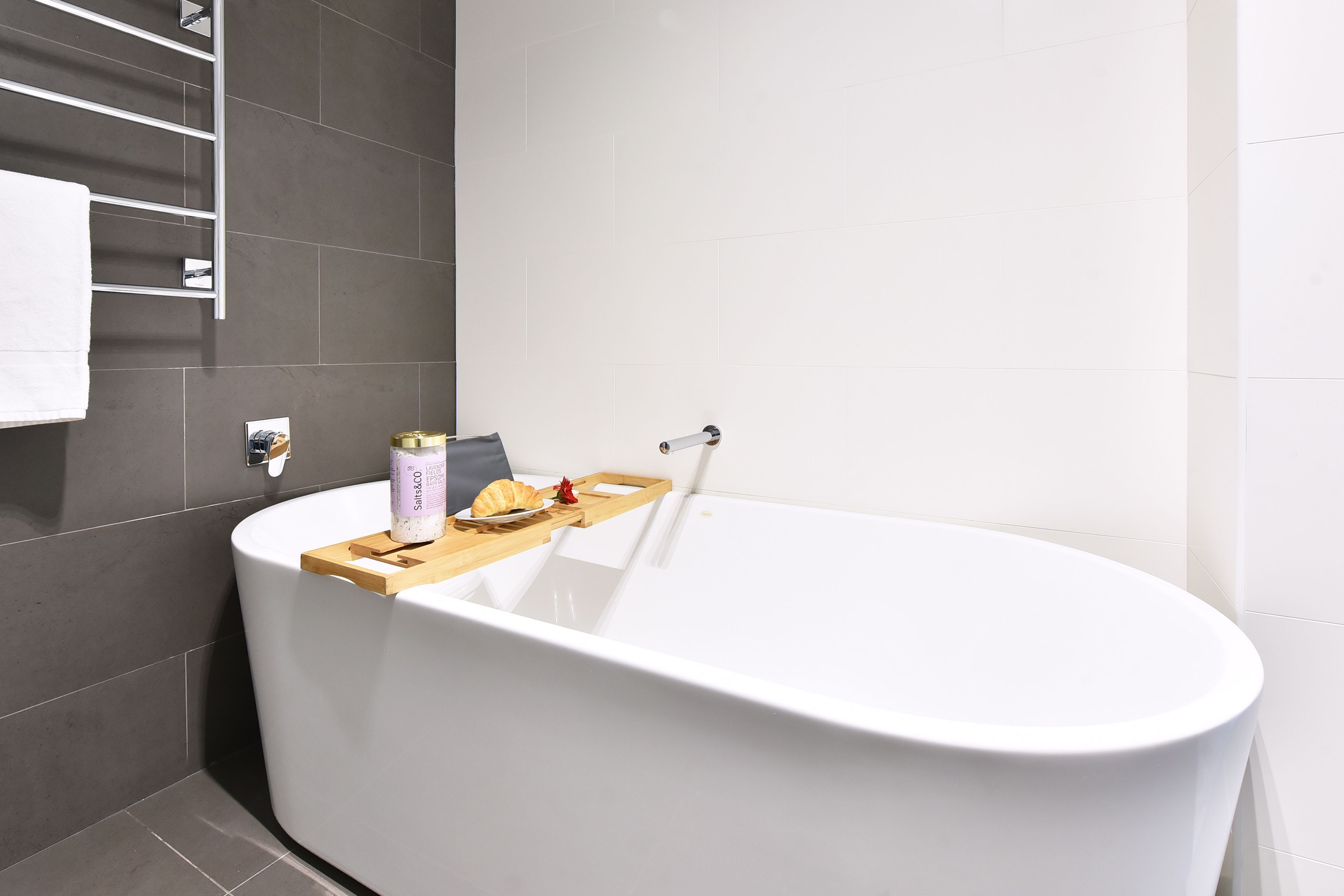 Une salle de bain moderne avec une baignoire sur pieds, un porte-serviettes et un petit plateau en bois contenant des articles de toilette.