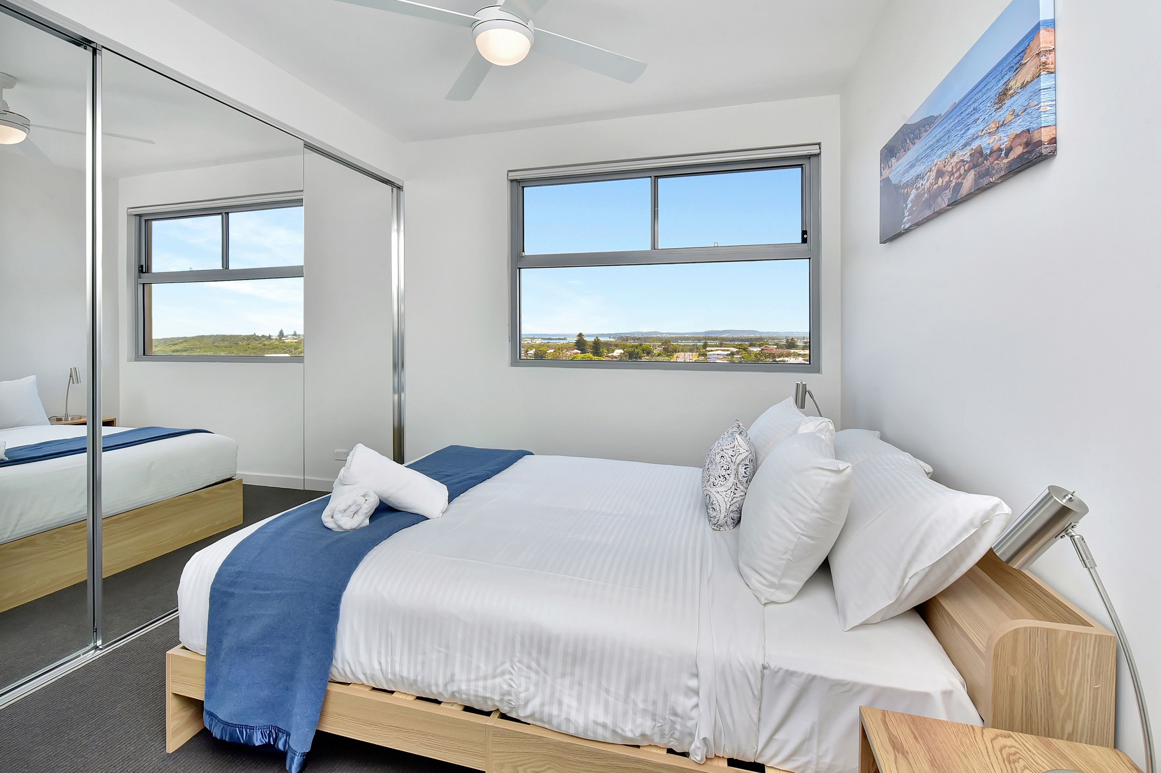A modern hotel room with a large bed, a ceiling fan, and a city view through the windows.