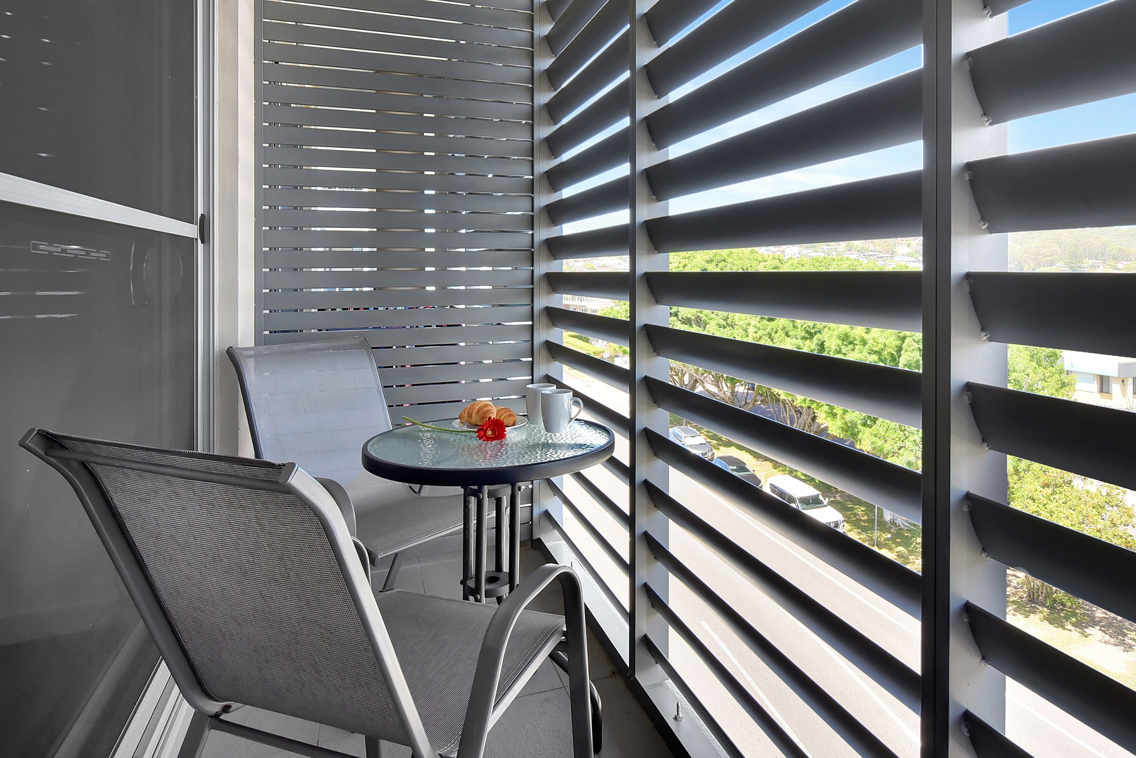 Un balcon avec une table et des chaises, une vue sur le paysage urbain et une fenêtre avec des stores horizontaux.