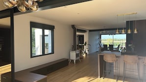 Una habitación amplia con un gran ventanal, una zona de comedor con taburetes de bar y una cocina con estufa.