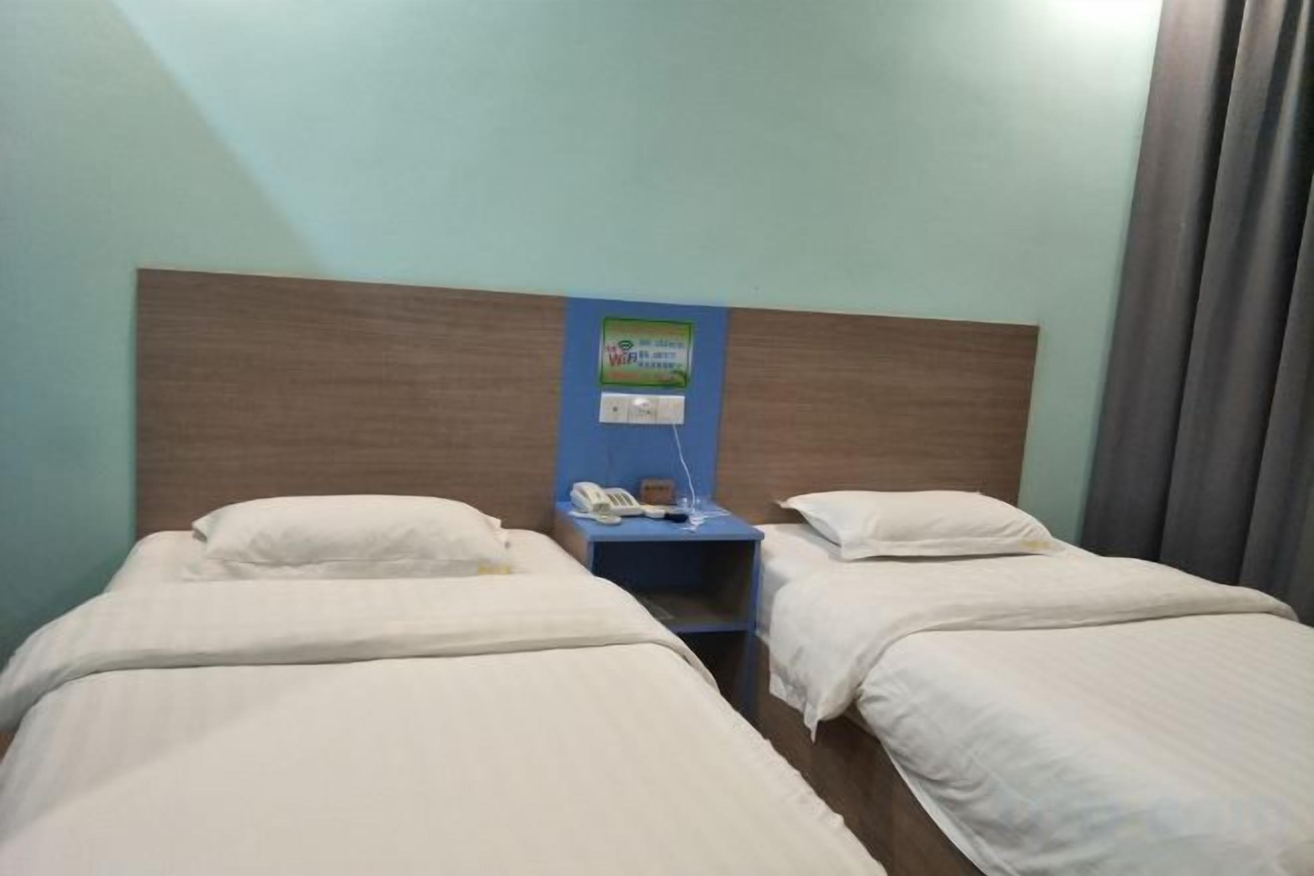 A hotel room with two beds, a nightstand with a phone, and a wall-mounted control panel.