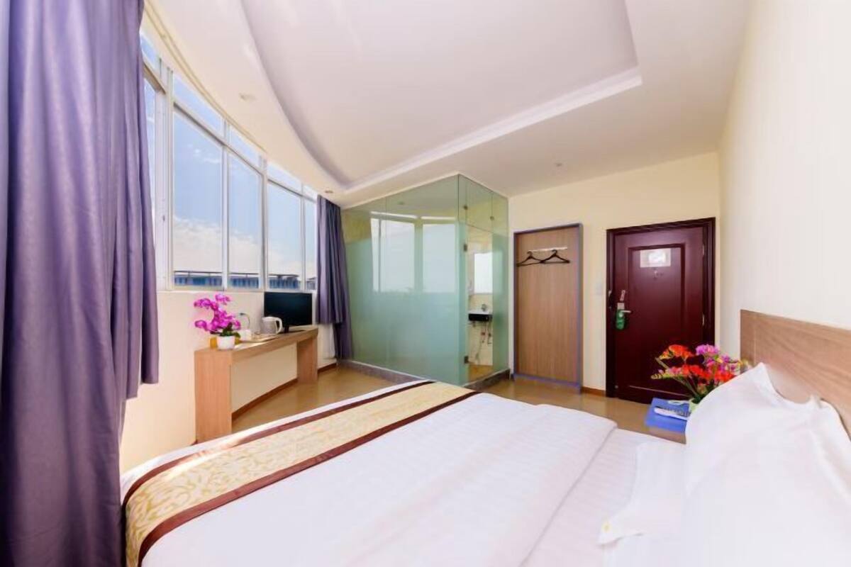 Une chambre d’hôtel avec un grand lit, un bureau avec un ordinateur, un miroir et une vue sur la ville.