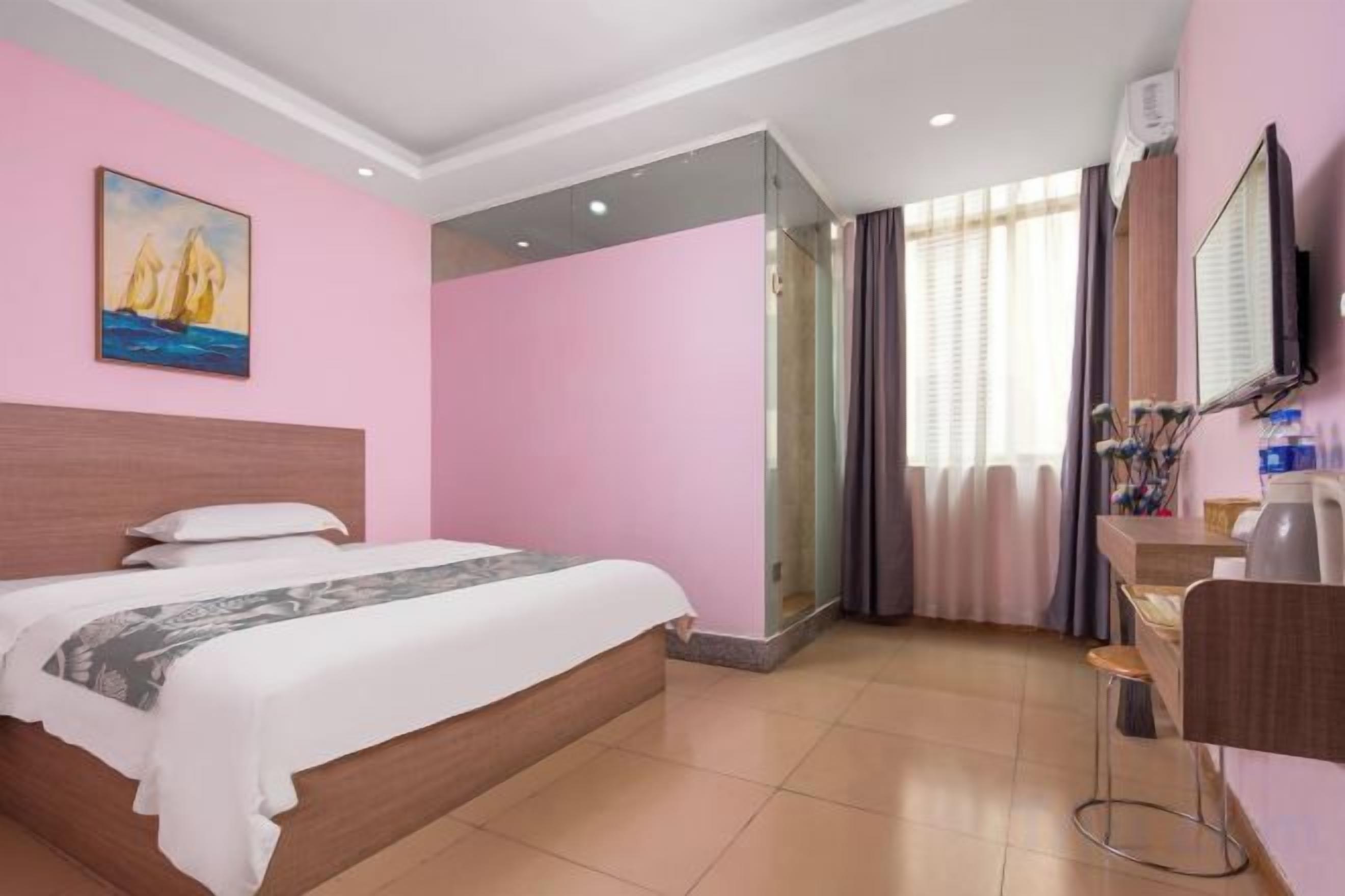 A hotel room with a bed, a desk, a chair, a mirror, and a window with curtains.
