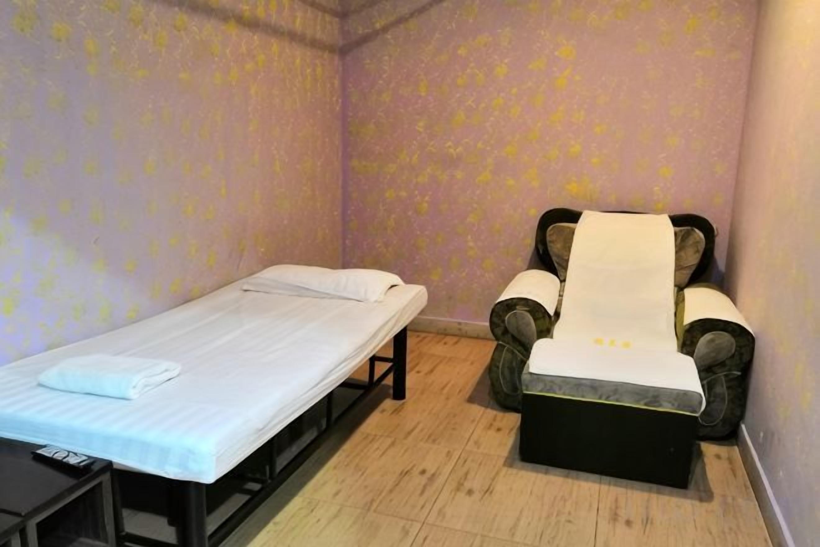 Una habitación individual con una cama, una silla de masaje y una pequeña mesa.