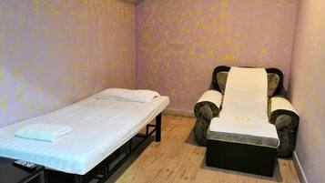 Una habitación individual con una cama, una silla de masaje y una pequeña mesa.