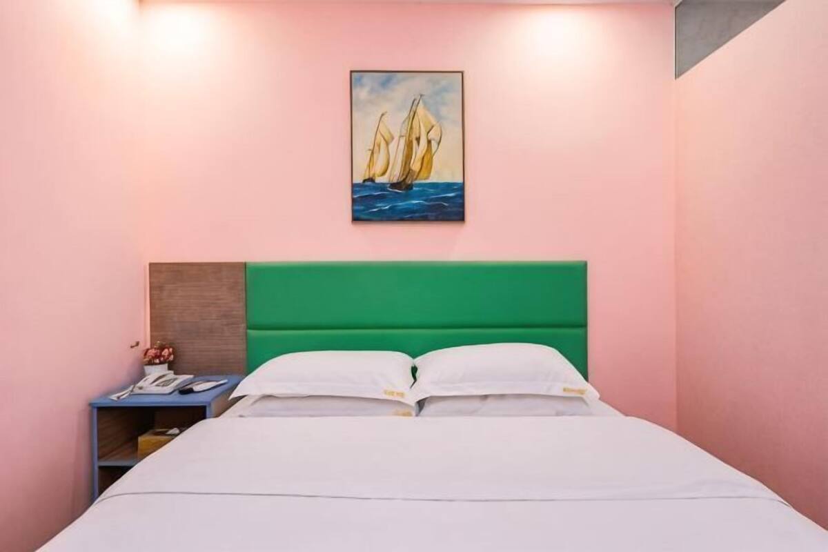 Un lit avec une literie blanche, une tête de lit verte et un tableau représentant des voiliers accroché au mur.
