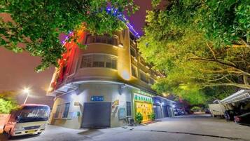 Un edificio de varios pisos con un espacio comercial en la planta baja, un área de estacionamiento y una calle arbolada.