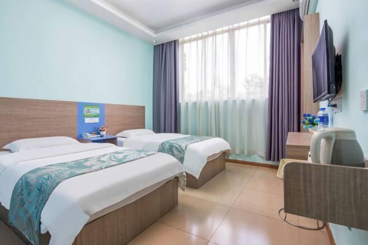 Une chambre d’hôtel avec deux lits, un bureau, une chaise, une télévision et une fenêtre avec des rideaux.