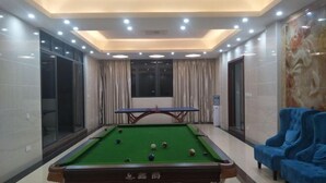 Une table de billard dans une pièce bien éclairée, dotée d’un plafond au design moderne et de fauteuils bleus.
