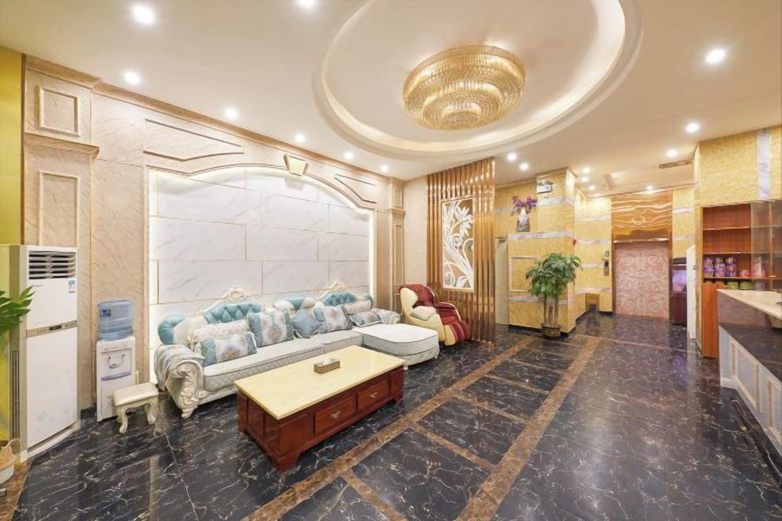 A hotel lobby with a marble floor, a sofa set, a reception desk, and a chandelier.