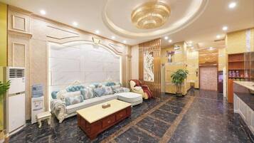 A hotel lobby with a marble floor, a sofa set, a reception desk, and a chandelier.