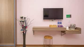A room with a television mounted on the wall, a wooden shelf with bottles and a kettle, and a vase with branches.