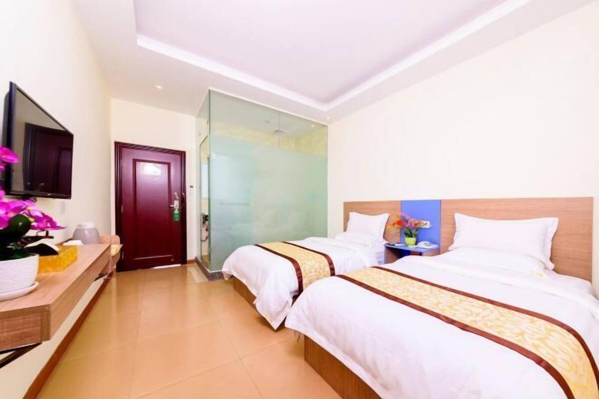 Une chambre d’hôtel avec deux lits, une télévision, un bureau en bois et une salle de bain avec une porte en verre.