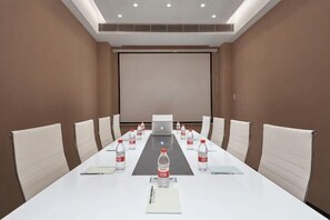Un salón de conferencias con una larga mesa, sillas, botellas de agua, una laptop y una pantalla de proyector.