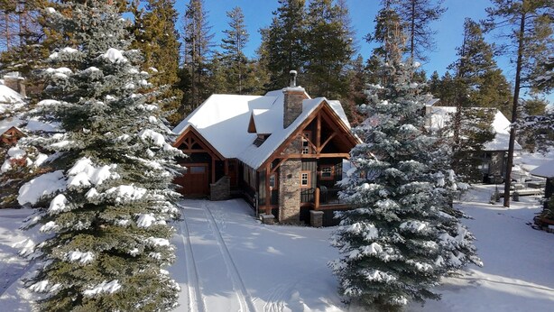 Una cabaña de troncos con techo cubierto de nieve, rodeada de árboles cargados de nieve.