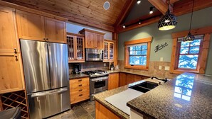 Una cocina con armarios de madera, electrodomésticos de acero inoxidable, encimeras de granito y salpicadero de piedra.