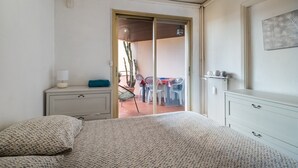 A bedroom with a bed, a nightstand, a dresser, a sliding glass door leading to a balcony with chairs and a table. - “Le Rose Garden” Apartment with Balcony, Wi-Fi, and Air Conditioning (Cagnes-sur-Mer)