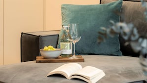 Un salon moderne avec un canapé gris, un coussin turquoise, une table d’appoint en bois sur laquelle se trouvent un livre, un verre et une bouteille.