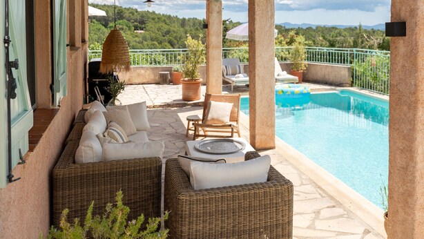 Ein überdachter Außenbereich mit Korbmöbeln, einem Pool und Blick auf die Landschaft.