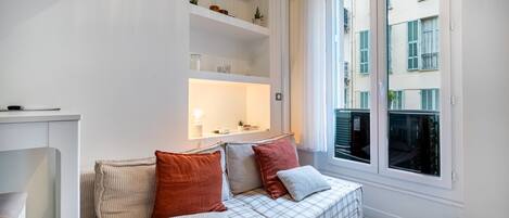 A modern living room with a sofa, shelves, and a window with a view of buildings.