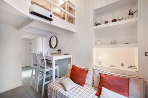 A modern living room with a dining area, a loft bedroom with a bed, and a white console table with decorative items. - Charming Studio in the Heart of Nice with Wi-Fi and Air Conditioning (Nice)